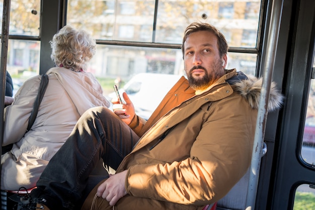 Man in public transport sitting with smartphone listening to music