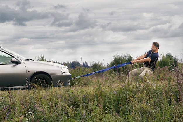 Photo man pulling his broken car using a tow rope along a country road