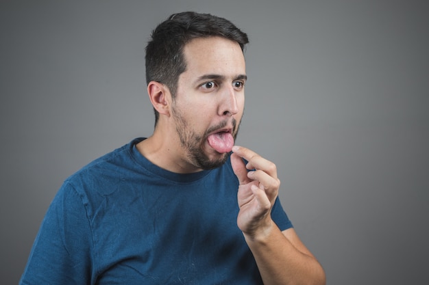 Man pulling something out of his tongue with a face of disgust