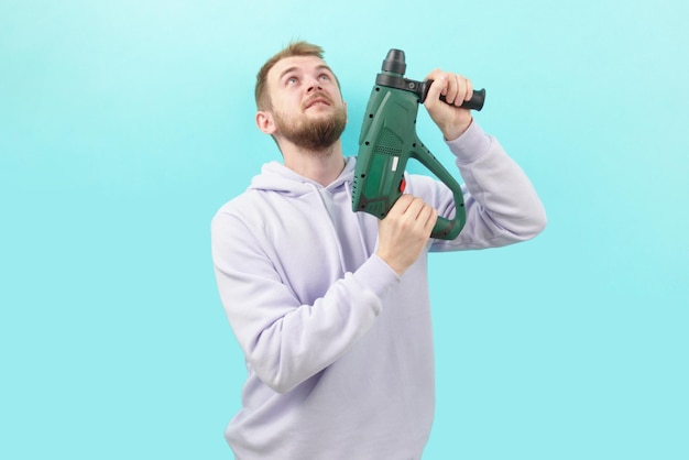 A man in a purple hoodie holding a drill on a blue background\
repairman working builder home improvement work tool apartment\
drilling indoors machine power renovation repair service