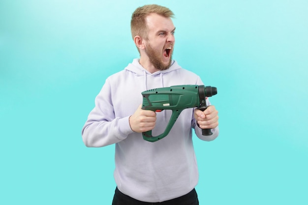 A man in a purple hoodie holding a drill and screaming crazy on a blue background Man Person Drill Holding Male Adult Tool Occupation One Person Repairman Working Builder Apartment Drill