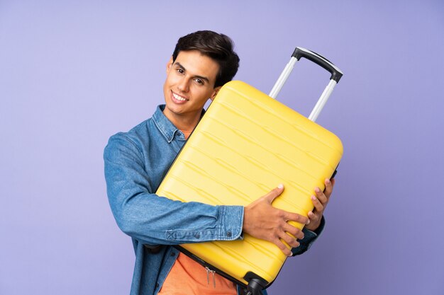 Man over purple wall in vacation with travel suitcase