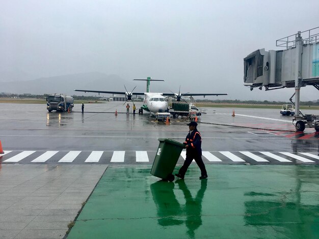 Foto uomo che spinge il bidone della spazzatura sulla pista dell'aeroporto durante la stagione delle piogge