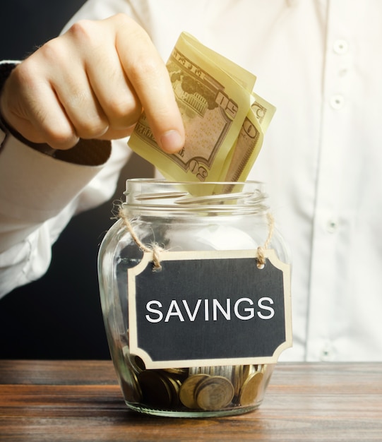 A man puts dollars in a glass jar Savings.