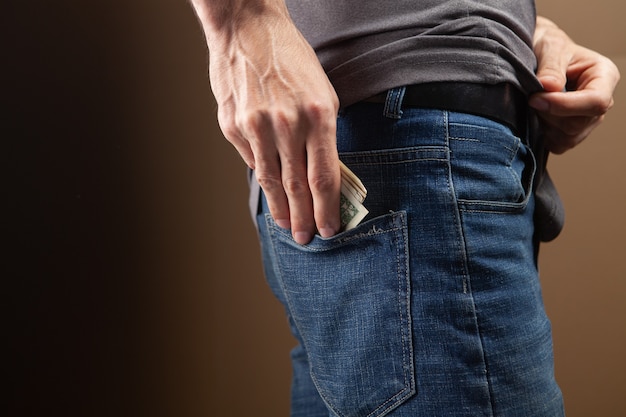 Man puts money in his back pocket on brown background