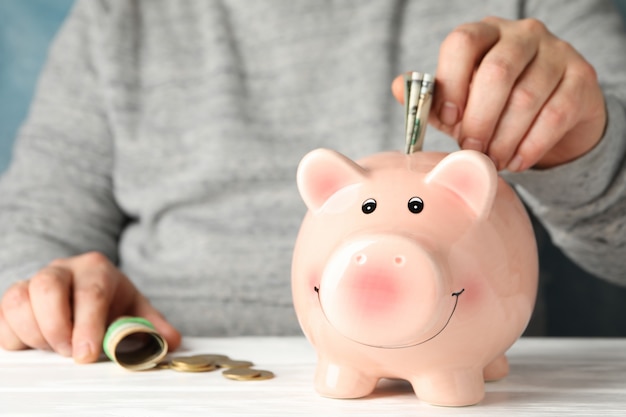 Man puts money in piggy bank on white wooden table