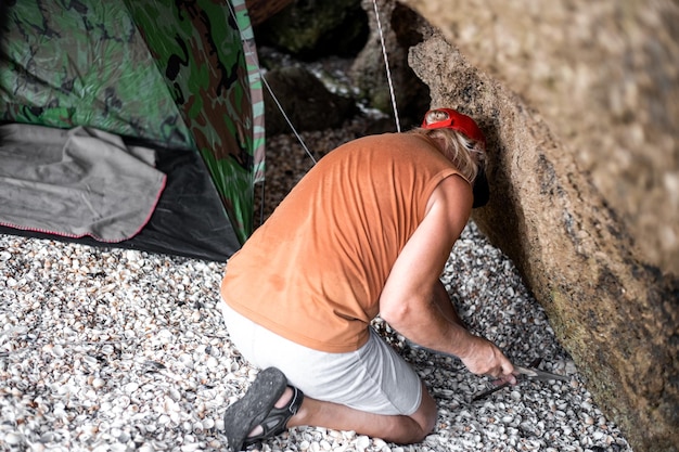 Un uomo monta una tenda turistica in una grotta di pietra in una giornata estiva viaggi e turismo