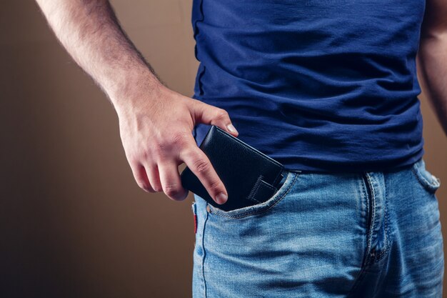 Man puts wallet in front pocket on brown background