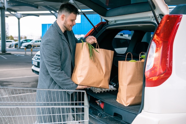 Человек кладет сумки с продуктом в копировальное пространство багажника автомобиля