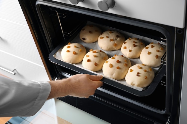 Man putting baking sheet with raw buns in oven