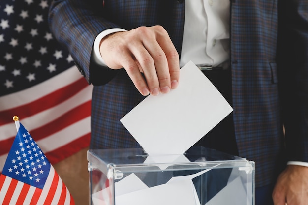 Foto uomo che mette scheda elettorale nella casella di voto contro la superficie marrone con la bandiera americana