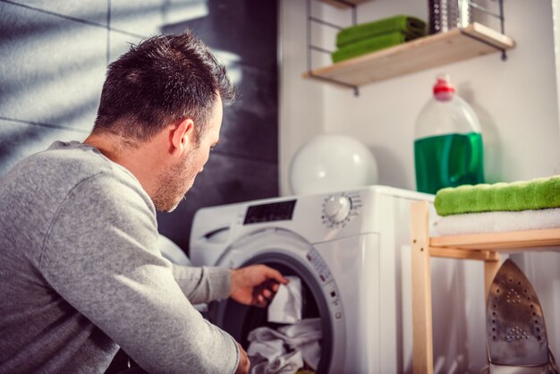 Uomo che mette i vestiti in lavatrice