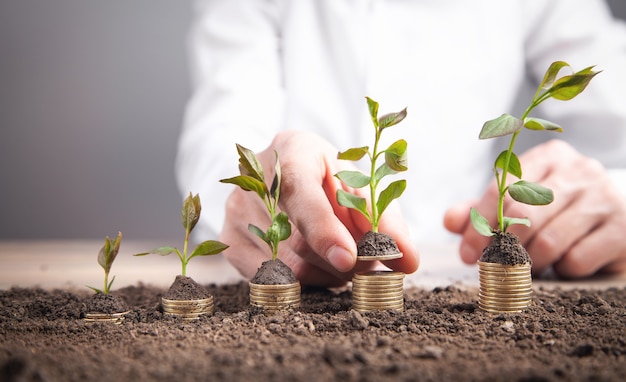 Man putting coin into rising stack of coins with plant.