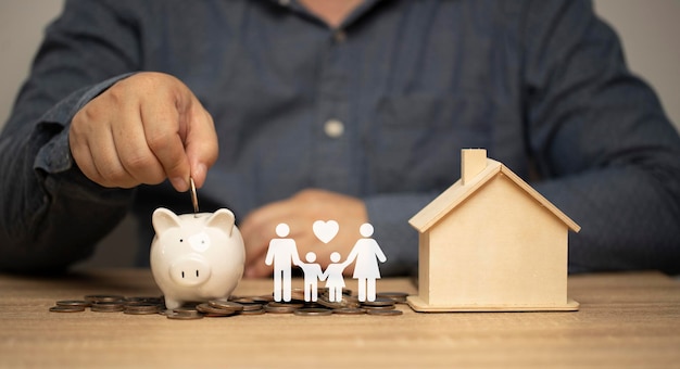 Man putting coin in piggy bank on table with family icon concept of saving for the future donating money long term investment finance planningloan buying a house