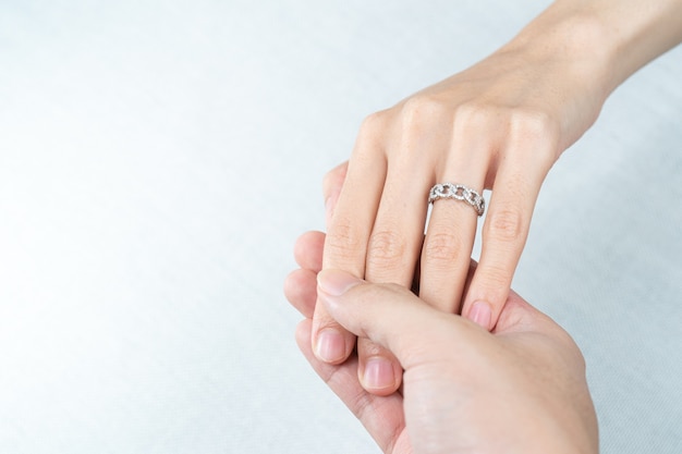 Man putting diamond ring on woman hand over white