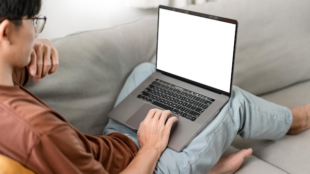 man putting on glasses leaning his back on the dark yellow while focusing on the laptop's screen