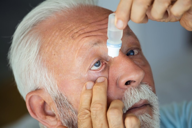 Мужчина капает жидкие капли в глаза, решая проблему со зрениемСтарший капает лекарство от глазных капель, исцеляя боль в глазах