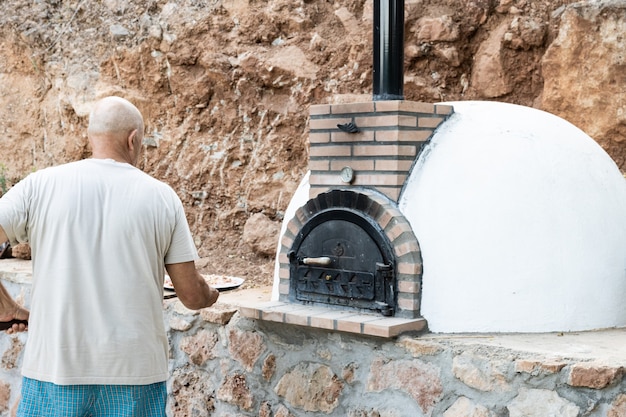 Uomo che mette la pizza nel forno a legna dipinto di bianco fatto a mano costruito all'aperto con la pala