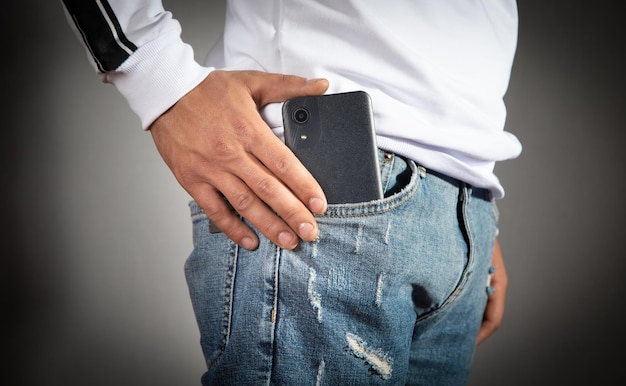 Мужчина кладет смартфон в карман джинсов