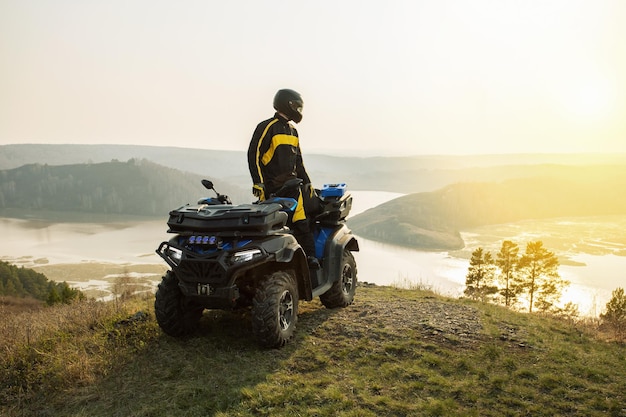 日没の冒険旅行で山のオフロードクワッドバイクATVに乗った男