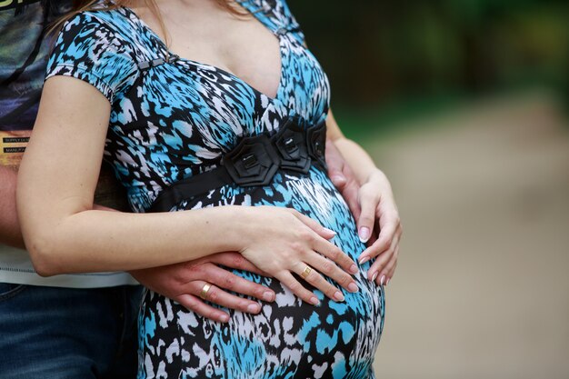 man raakt de buik van de zwangere vrouw buitenshuis. twee handen op zwangere vrouwenbuik sluiten omhoog. mooie paar wachten op een bevalling. gelukkige jonge familie wachten baby. 9 maanden gezonde zwangerschap.