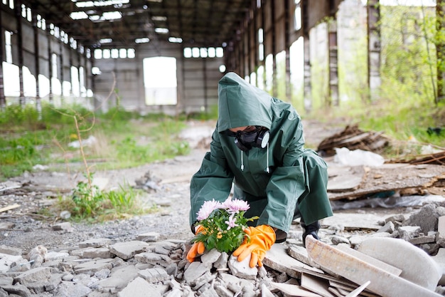 Мужчина в плаще и противогазе собирает цветок с выжженной токсичной земли Концепция загрязнения воздуха Экологическая катастрофа