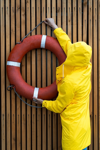 Man in raincoat hanging a red lifebuoy on a wooden wall