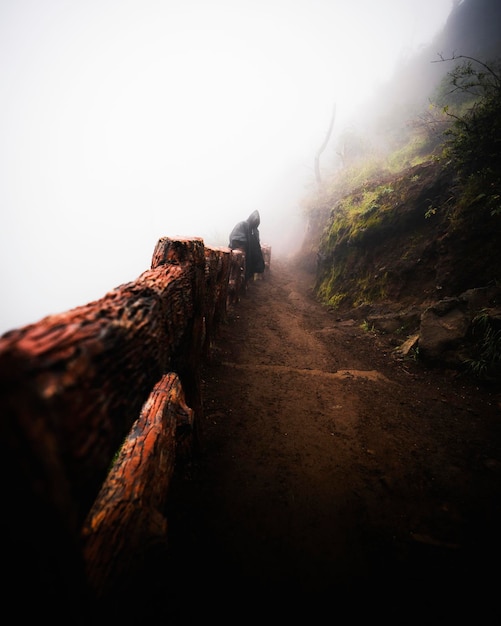 Man in a raincoat sitting on a wooden fence on a steep dirt road