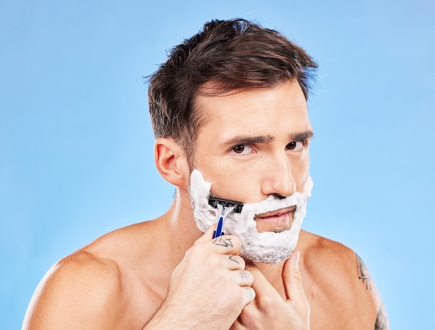 Man razor and shaving for haircare grooming and hair removal for hygiene on a blue studio background Portrait man and beauty to shave beard or face with foam or soap for facial cleansing