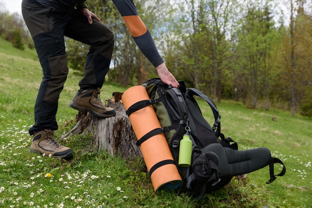 A man reaches for a backpack that lies on the grass rest rest