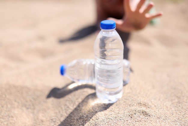 Man reaches for bottle of water standing on sand