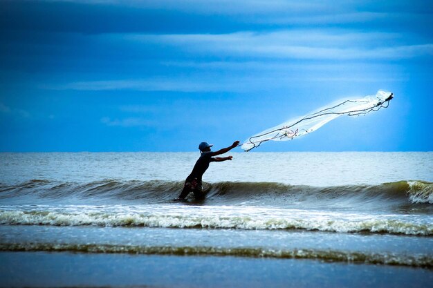 Photo man reaching fishing net in sea against sky