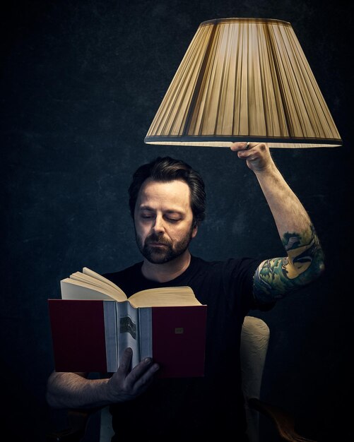 Foto uomo che legge un libro davanti a una lampada illuminata