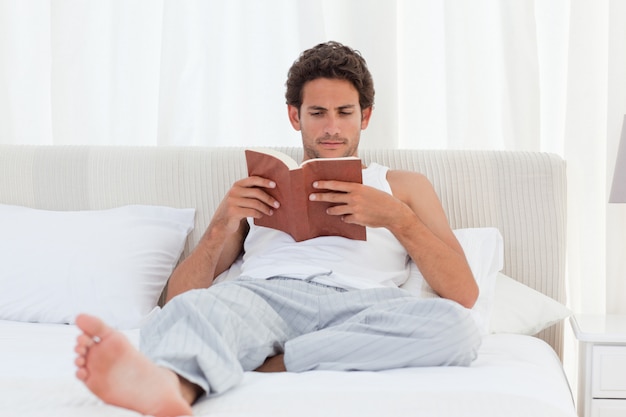 Man reading a book on his bed 