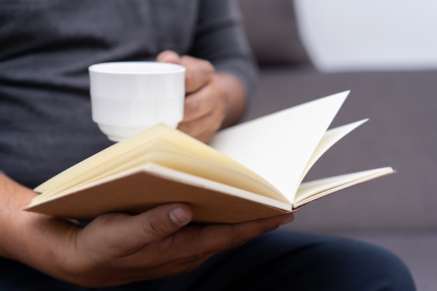 Uomo che legge un libro e tiene una tazza di caffè sit read knowledge