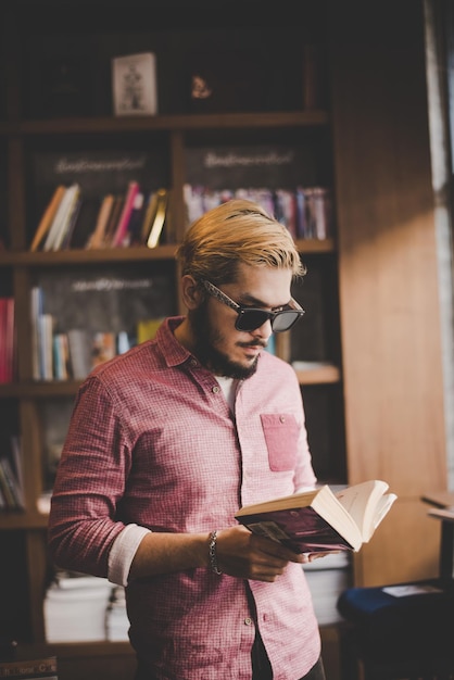 man reading book while standing in cafe