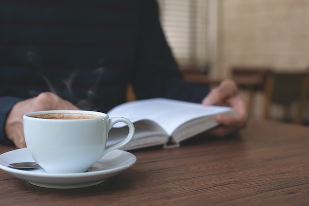 man reading a book on wooden table at coffee shop