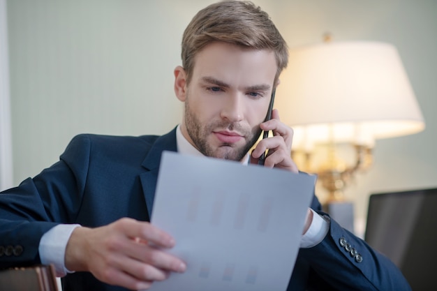 A man reading a business report and making a phone call