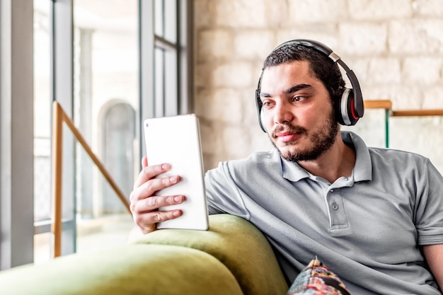 Man reading an e book on tablet sitting on a comfortable couch at home