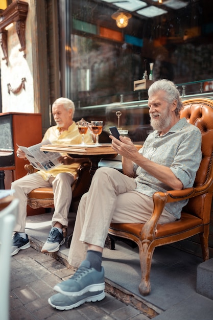 Messaggio di lettura dell'uomo. uomo in pensione barbuto che legge un messaggio sullo smartphone mentre è seduto fuori con un amico