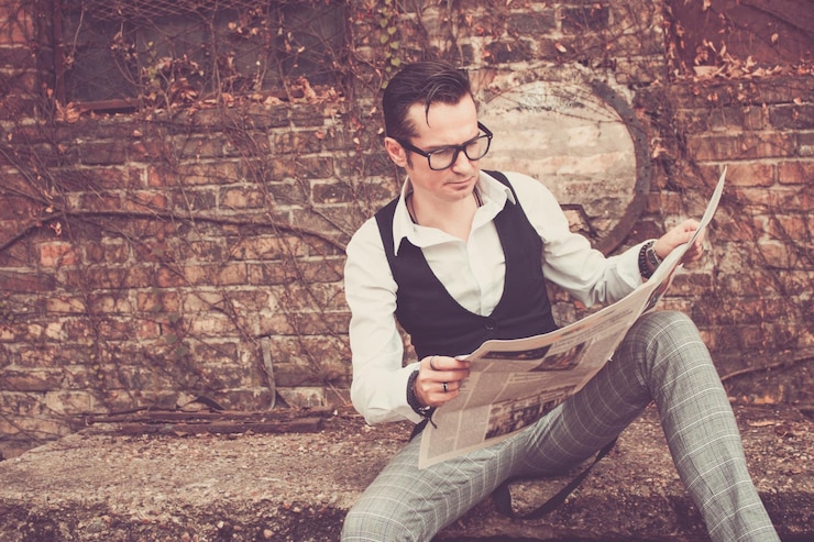 फोटो man reading newspaper while sitting against wall