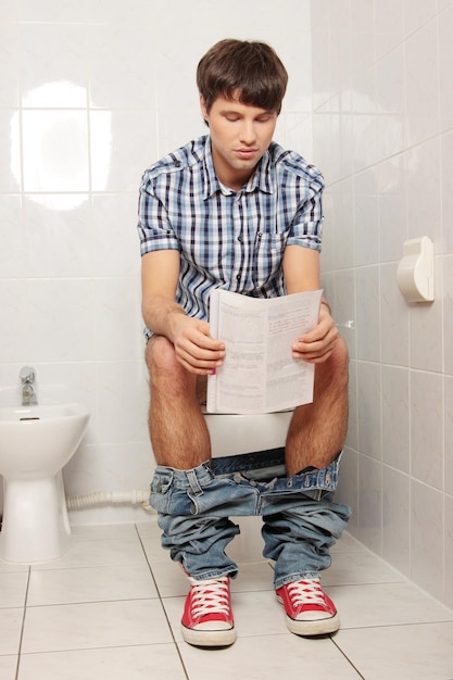 Photo man reading paper while sitting on toilet bowl at home