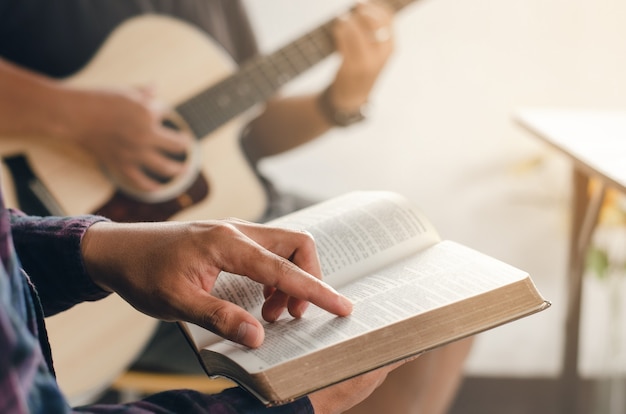 Man reads a Bible while his friends play guitar close up