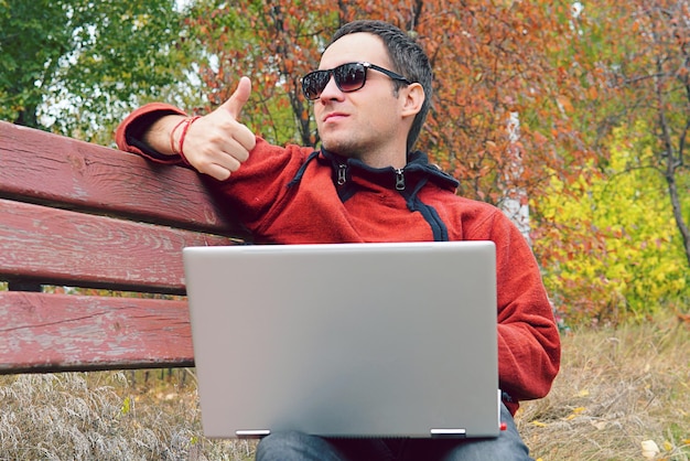 A man reads messages news on the ultrabook and shows a finger up That is all right Happy young man or male hipster in casual wear relax sitting on holding digital pc modern lifestyle concept