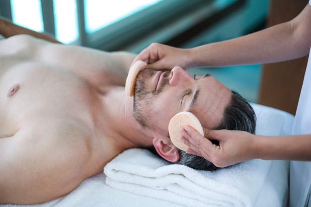 Man receiving a facial massage from masseur 