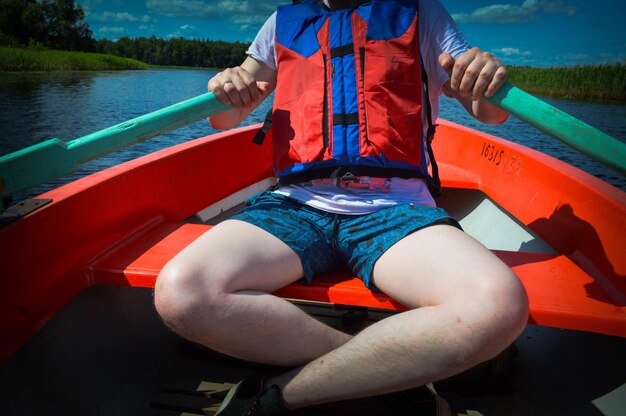 A man in a red boat shorts and a life jacket is paddling with oars on a boat for a walk