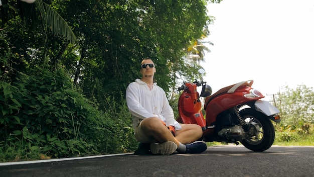 L'uomo sulla moto rossa in abiti bianchi guida il viaggio su strada forestale un turista caucasico di uomini