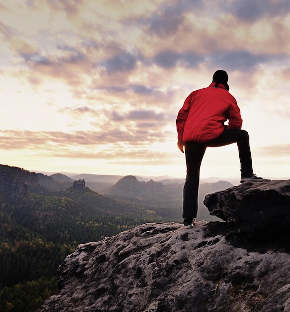 Photo man in red outdoor jacket on sharp cliff mountains within early fall daybreak conceptual scene