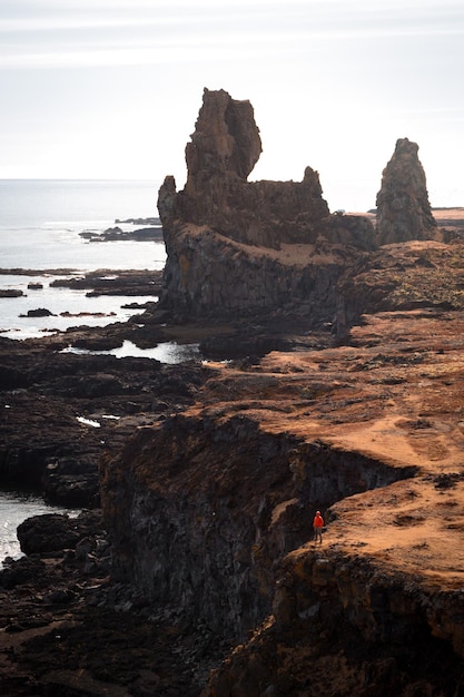 Foto un uomo vestito di rosso si trova su una scogliera a picco sull'oceano.