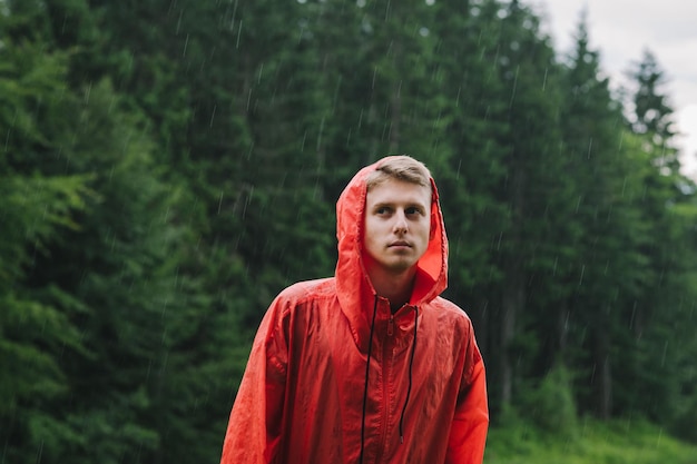 man in a red raincoat in the mountains in the rain looks into the camera with a serious face